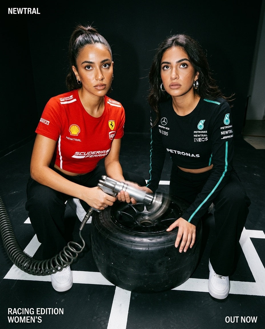 Ferrari Scuderia Women's Crop Tee (Red) and Mercedes-AMG Petronas Women's Longsleeve Crop (Black) bundle: Both models crouching around an F1 wheel with impact wrench, both garments fully visible, pit-lane floor markings