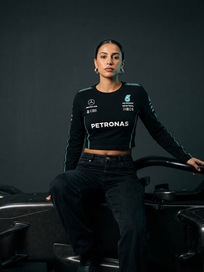 Newtral Mercedes-AMG Petronas women's long-sleeve top in black, model sitting on a Mercedes F1 car