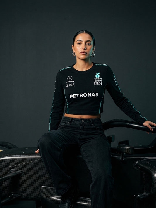 Newtral Mercedes-AMG Petronas women's long-sleeve crop top in black, model sitting on a Mercedes F1 car